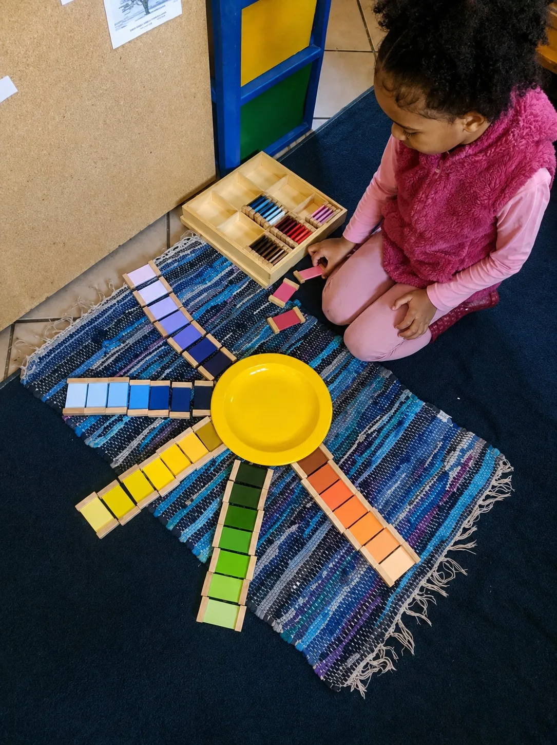 A child arranging Montessori colour tablets into a bright sunburst pattern